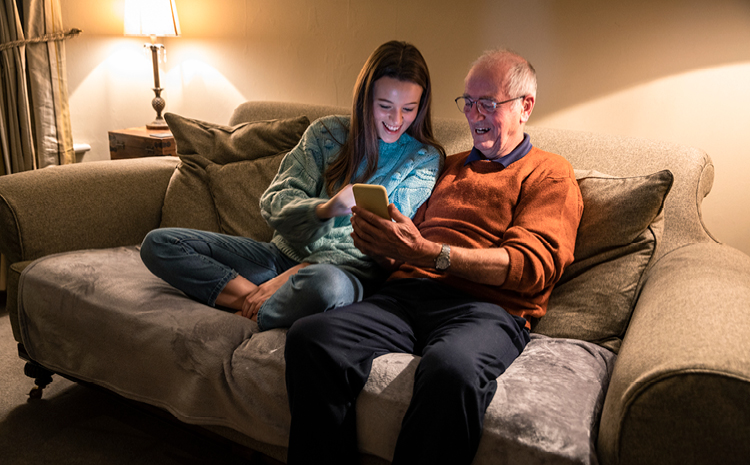 An elderly man and his granddaughter sitting on a couch looking at a phone