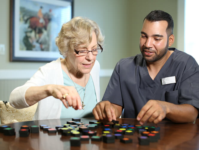 an older woman and a male worker playing a board game in memory care