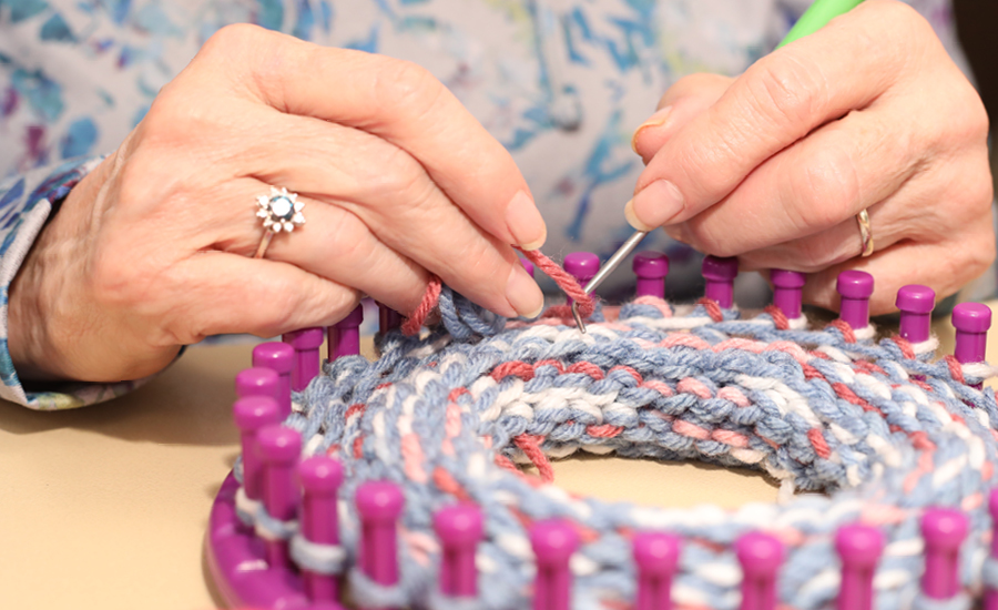 close up of woman as she uses a loom to knit hat 