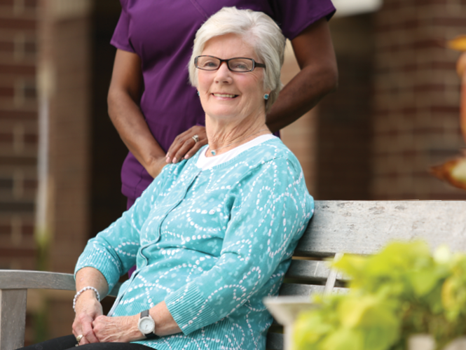 senior woman relaxes on bench with healthcare worker nearby