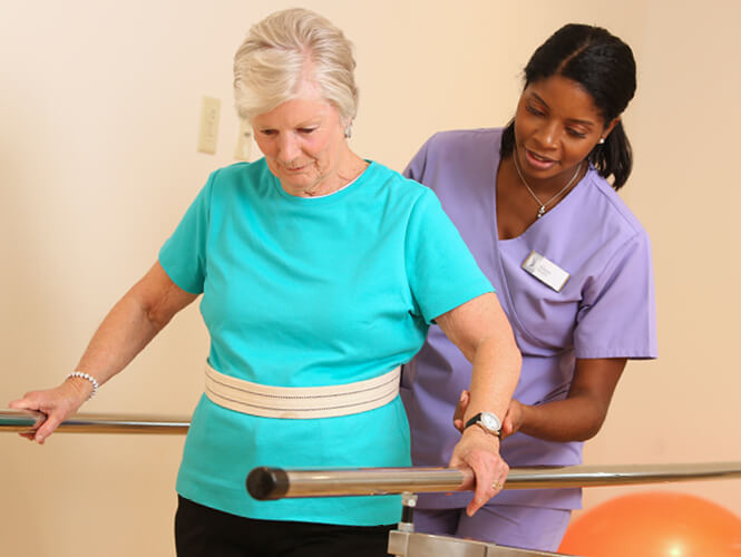 rehab therapist assists senior woman with gait belt