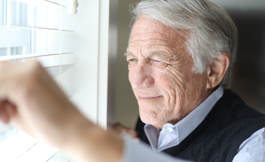 senior man looks out window blinds