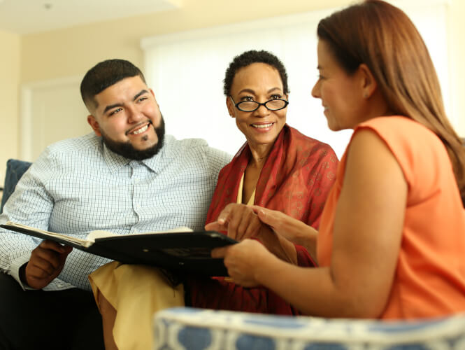 A young man and his senior mom look at a booklet with a female healthcare staff