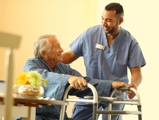 Male CNA helps senior man stand with his walker