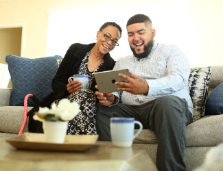 A man and a woman on a couch smiling while looking at an ipad at victorian village