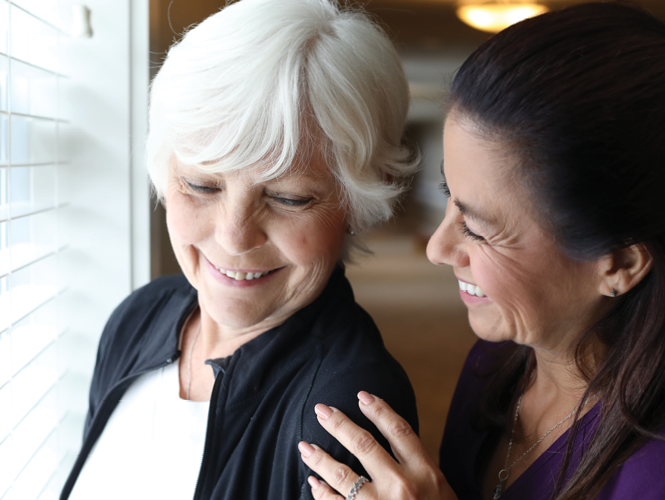 senior woman enjoys view out window as female healthcare worker speaks to her